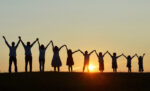 Group of people with hands held high before a sunset